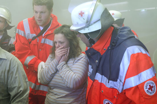 Foto: Zwei Helfer kümmern sich um eine Frau, die schockiert an einem Einsatzort steht.